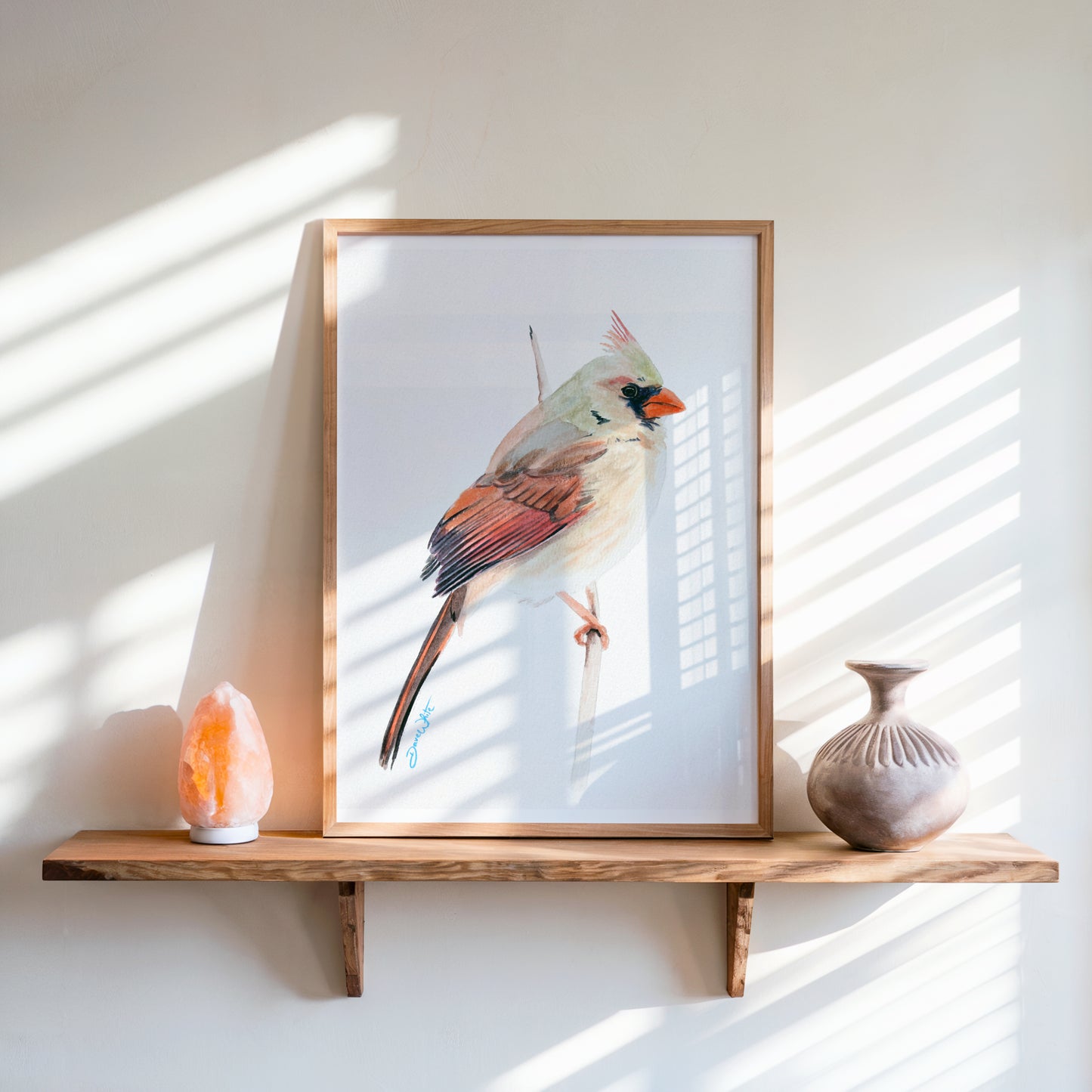 Framed artwork of a female cardinal bird on a wooden shelf with decorative items.