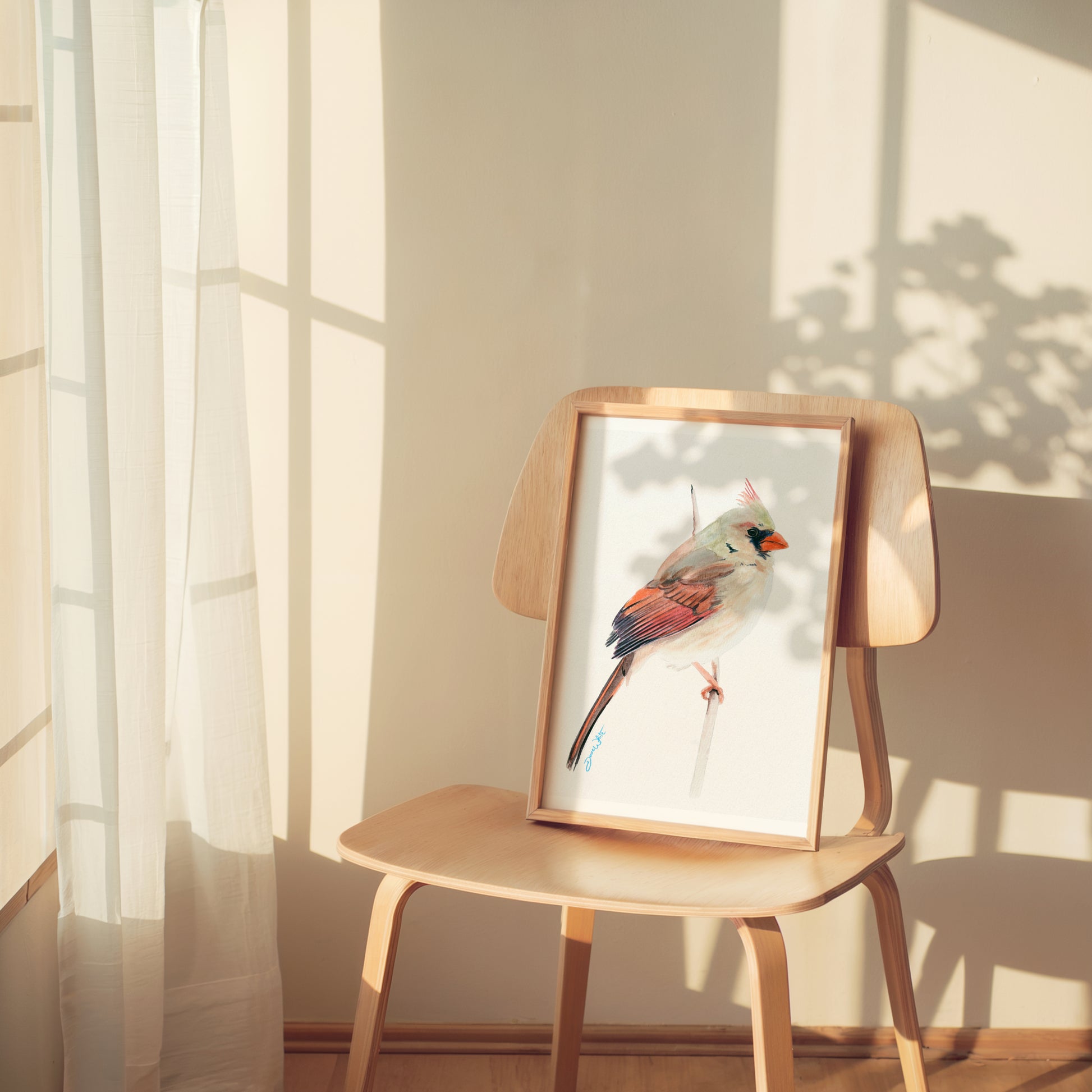 Framed artwork of a female cardinal bird on a wooden chair with sunlight filtering through curtains.