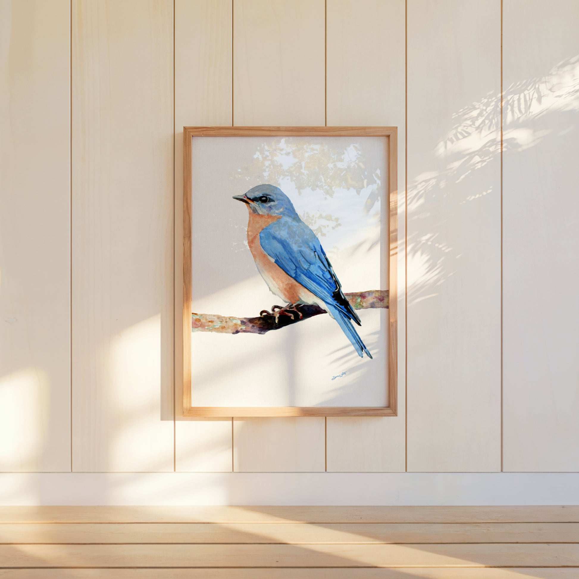 Framed artwork of a female blue bird on a white background, hanging on a light wooden paneled wall.