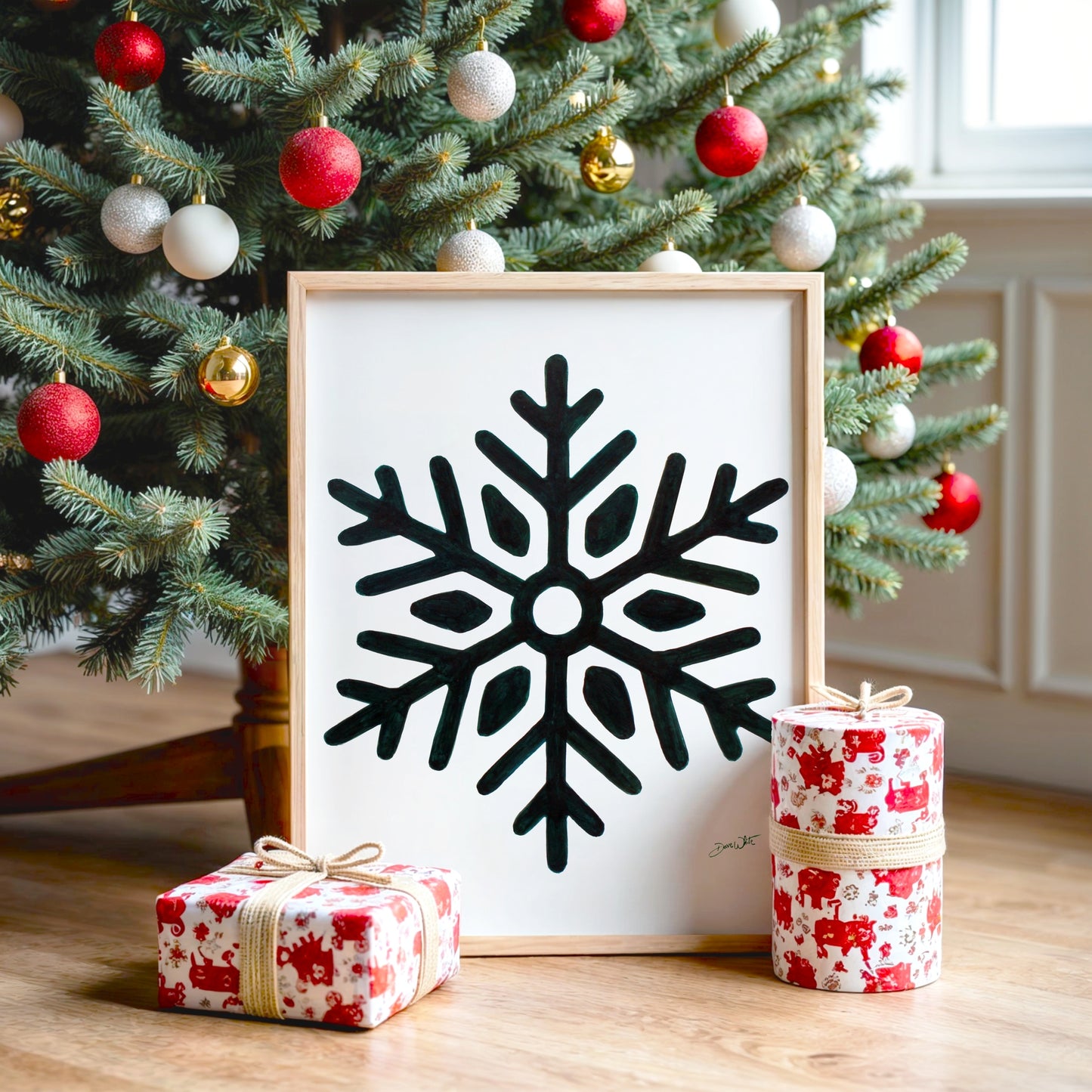 Framed dark green snowflake art piece on a table with Christmas tree and presents in the background