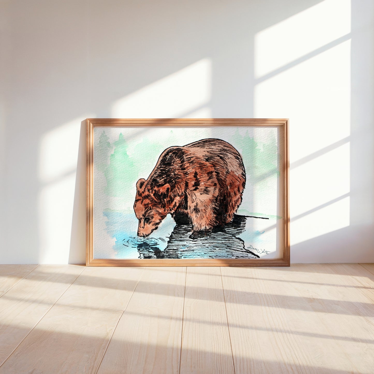 Framed artwork of a bear drinking water on a light wooden floor with a white wall background