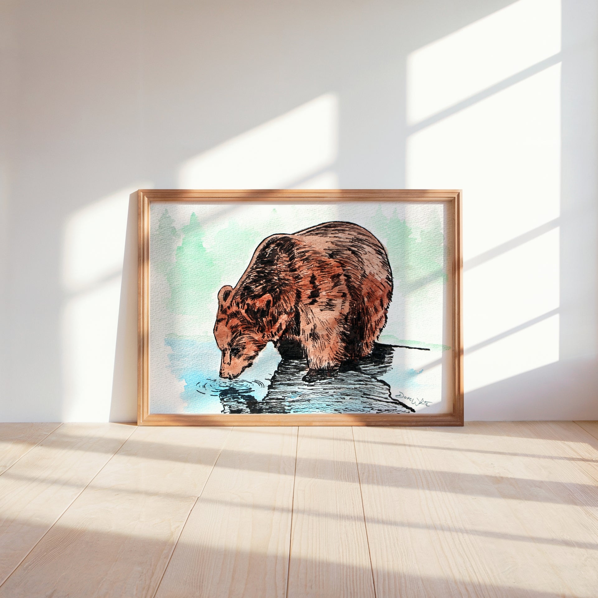 Framed artwork of a bear drinking water on a light wooden floor with a white wall background