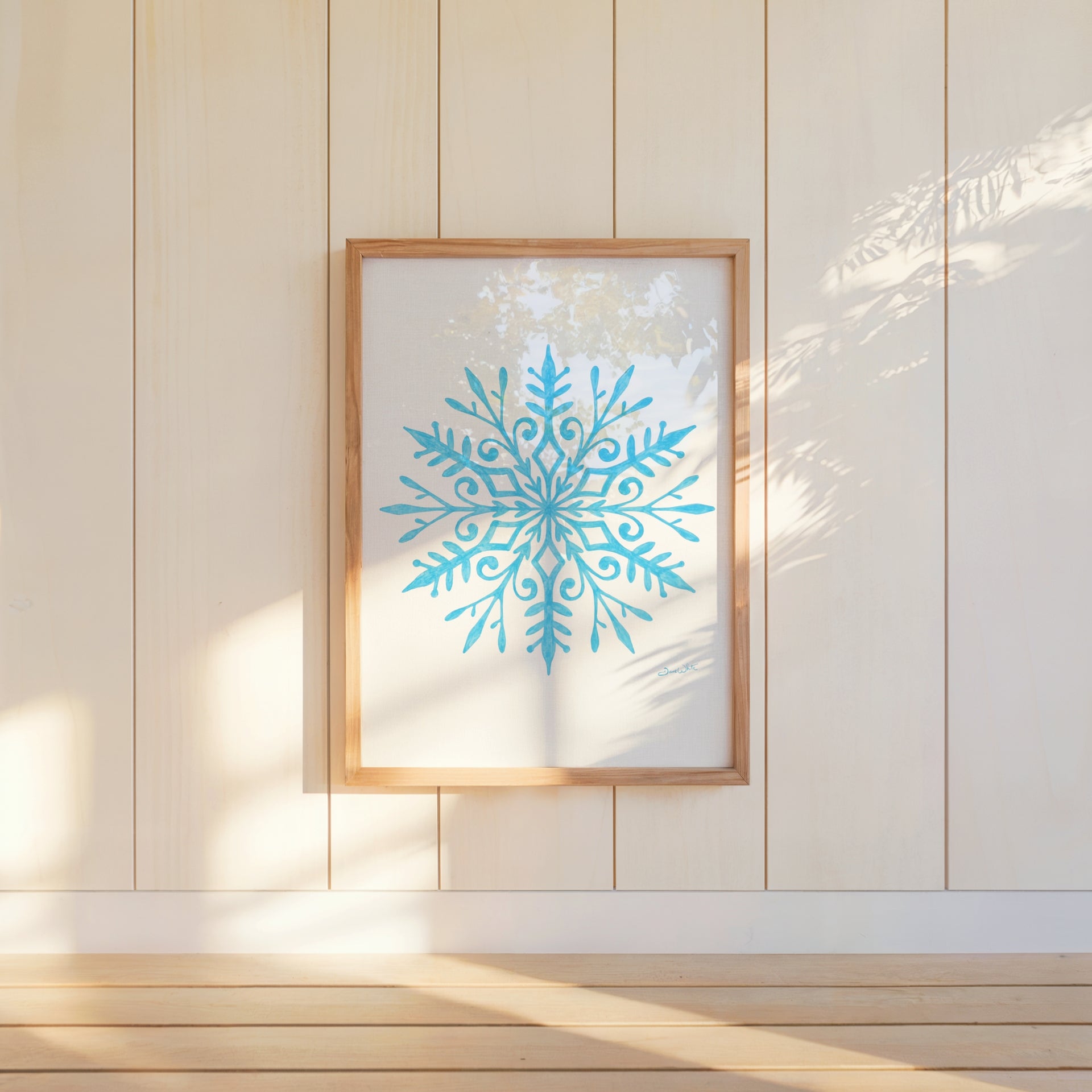 Framed artwork of a blue snowflake on a light wooden panel wall.