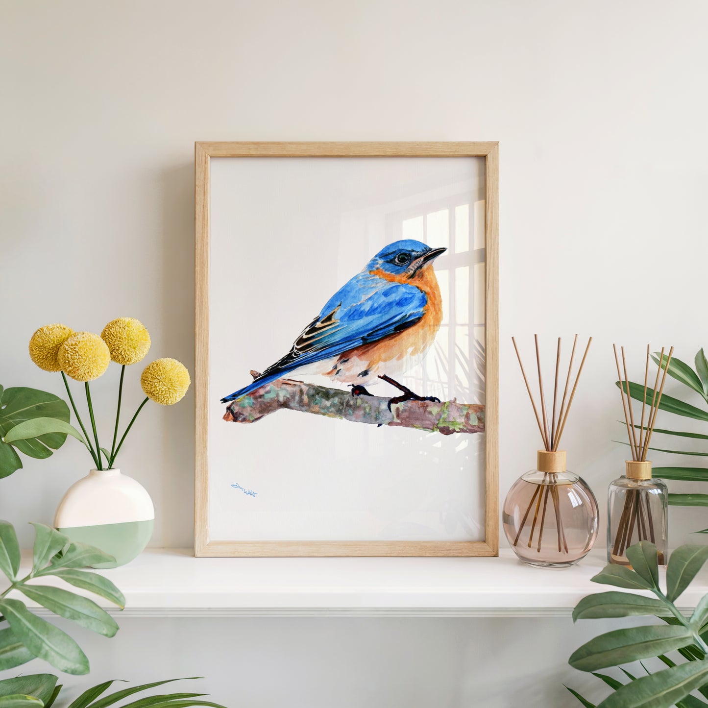 Framed artwork of a blue bird on a branch with decorative items on a shelf.
