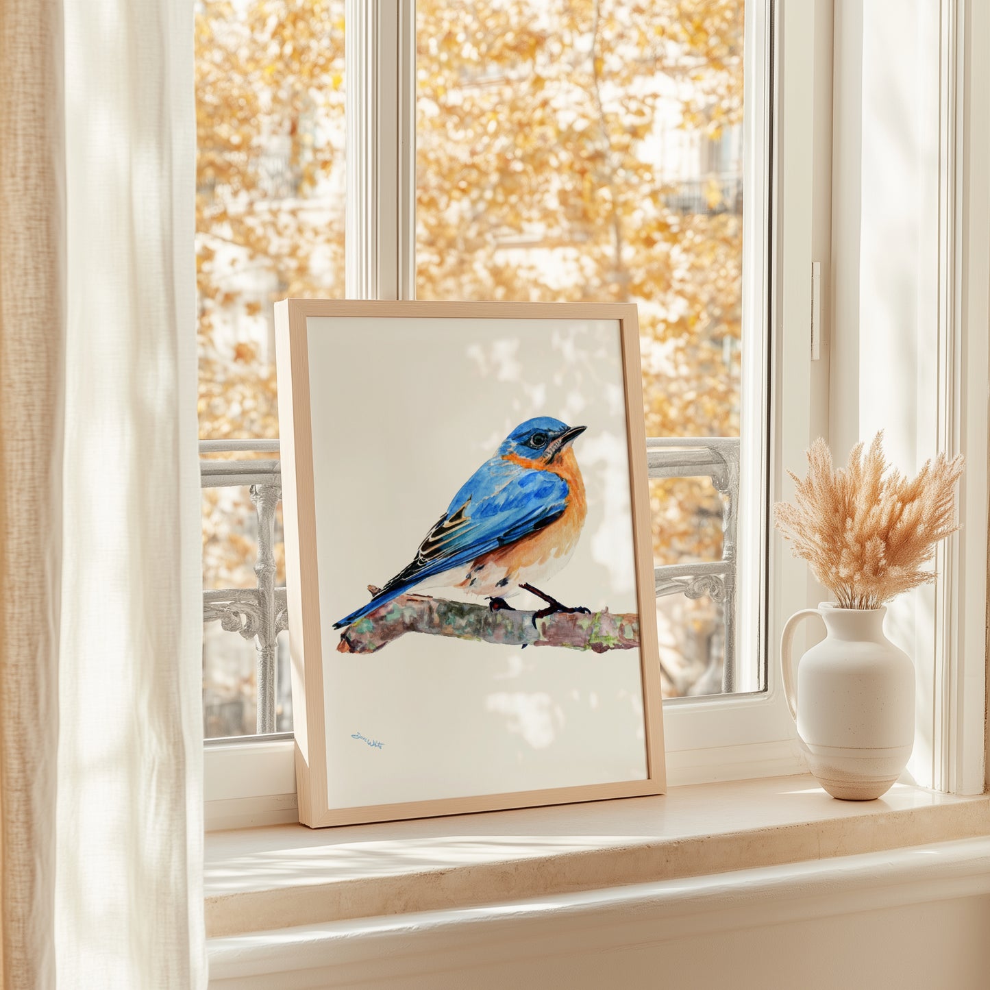 Framed artwork of a blue bird on a branch in front of a window with autumn foliage.