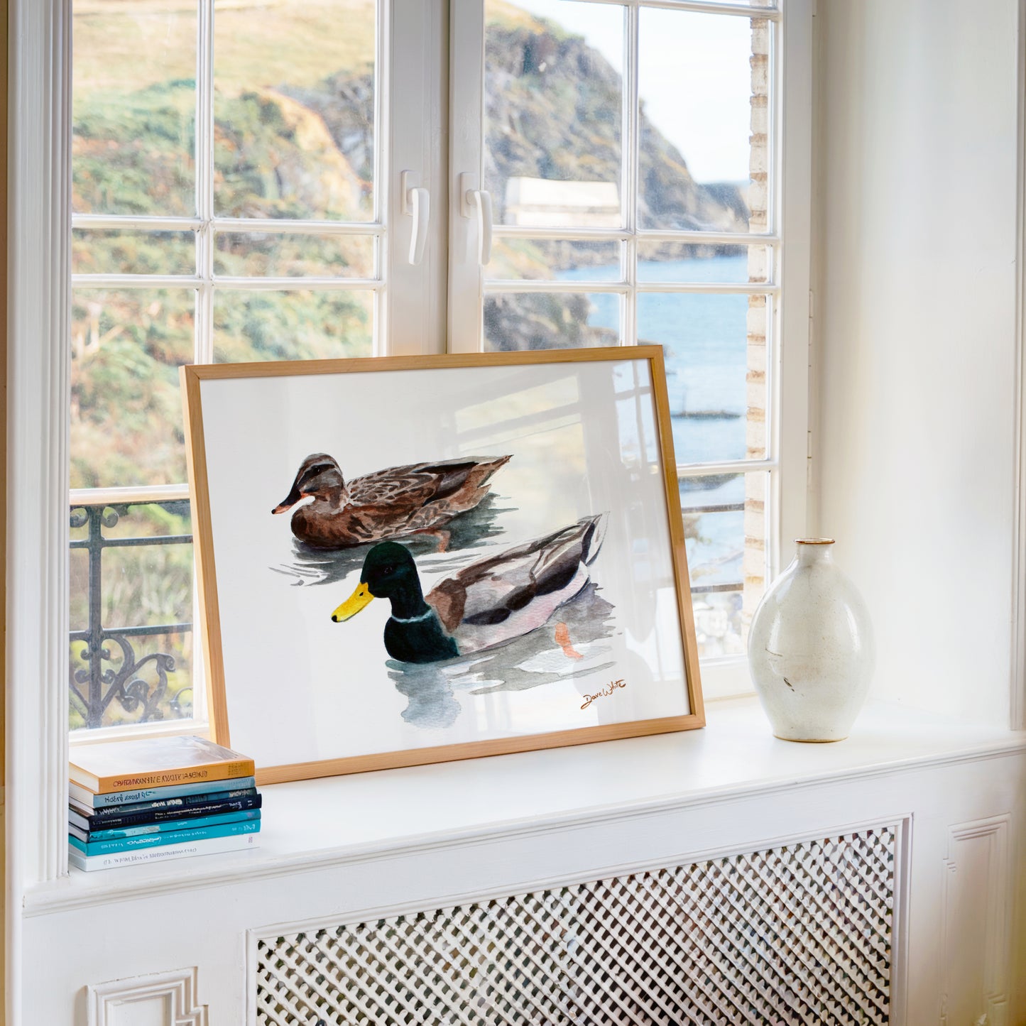 Framed artwork of two ducks on a windowsill with a scenic view outside.